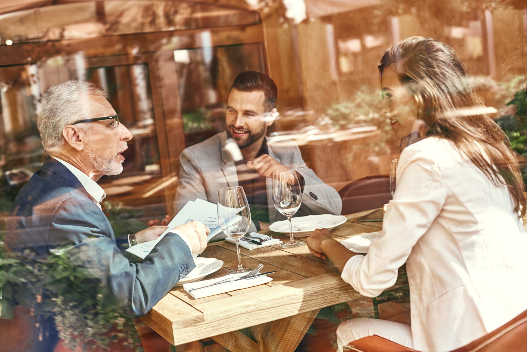 Tres personas comiendo en un restaurante mientras mantienen una reunión de negocios